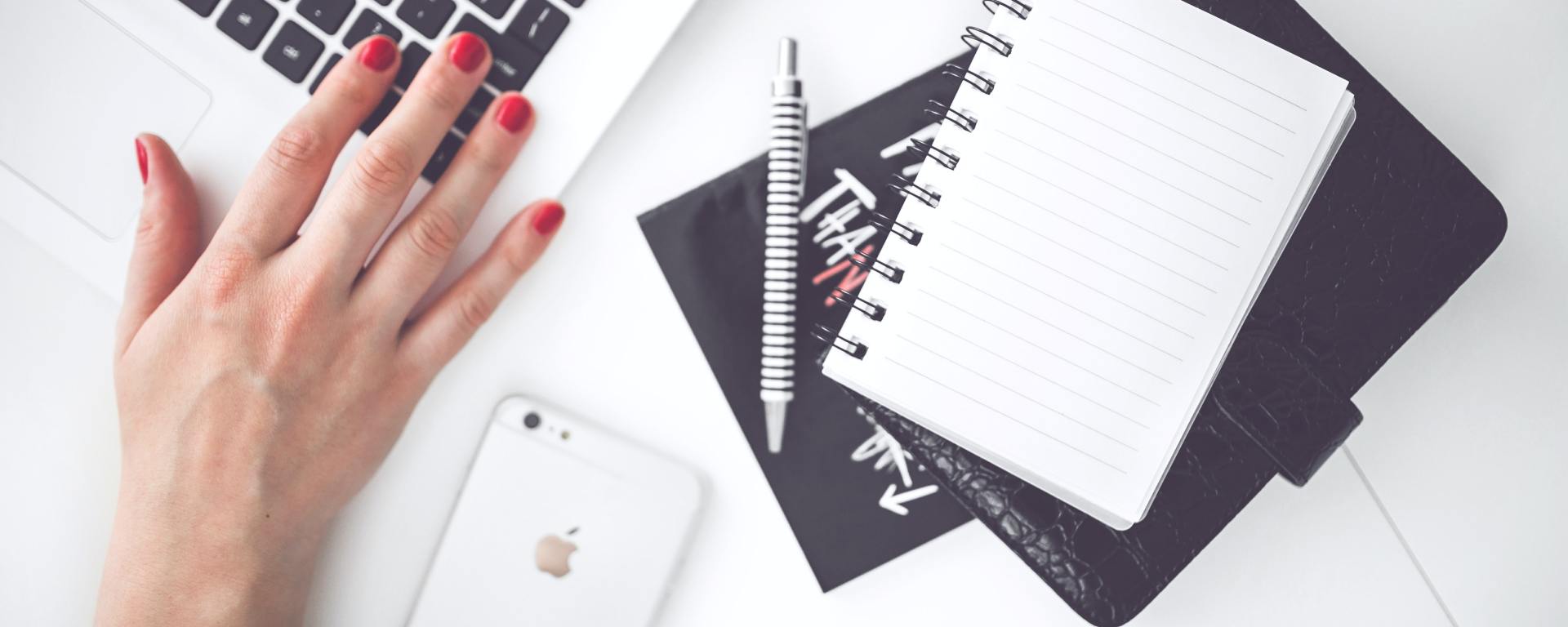 laptop, notebooks, phone, pen, and hand with painted nails
