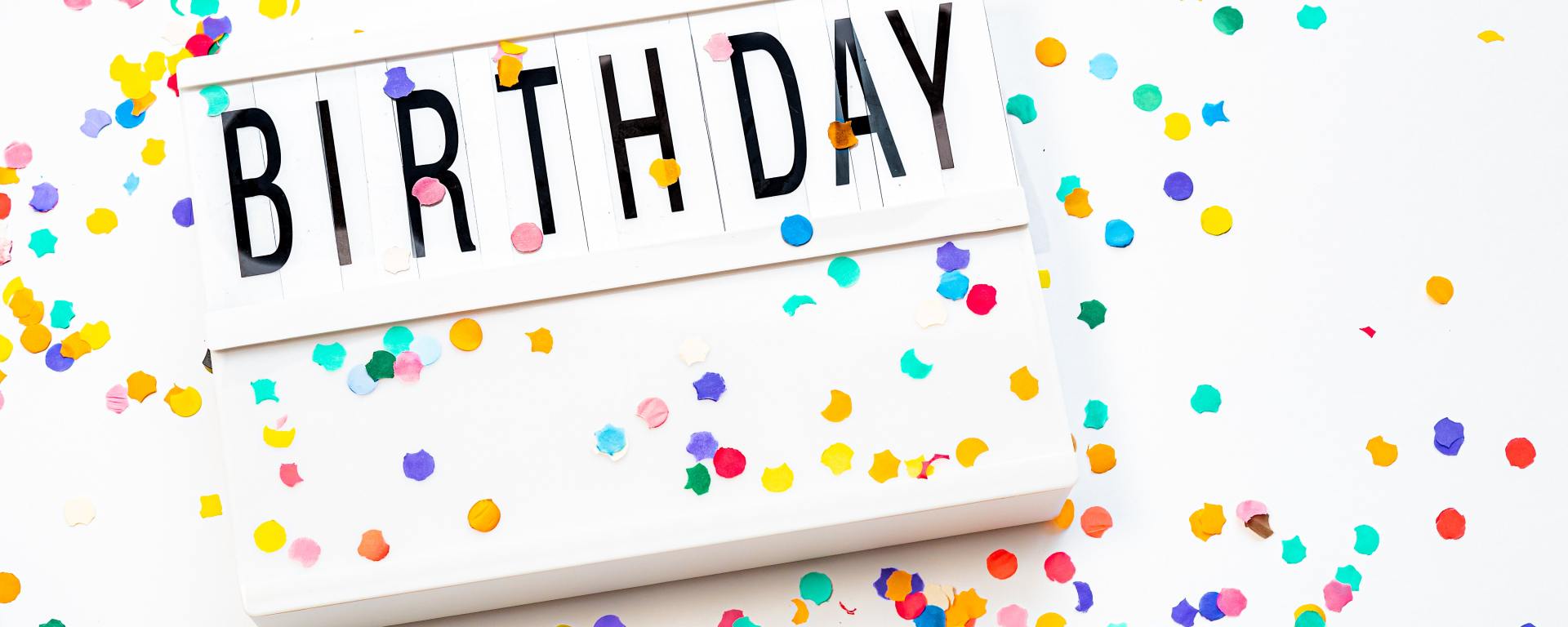 white sign that reads "birthday" in black letters surrounded by colorful confetti on a white background
