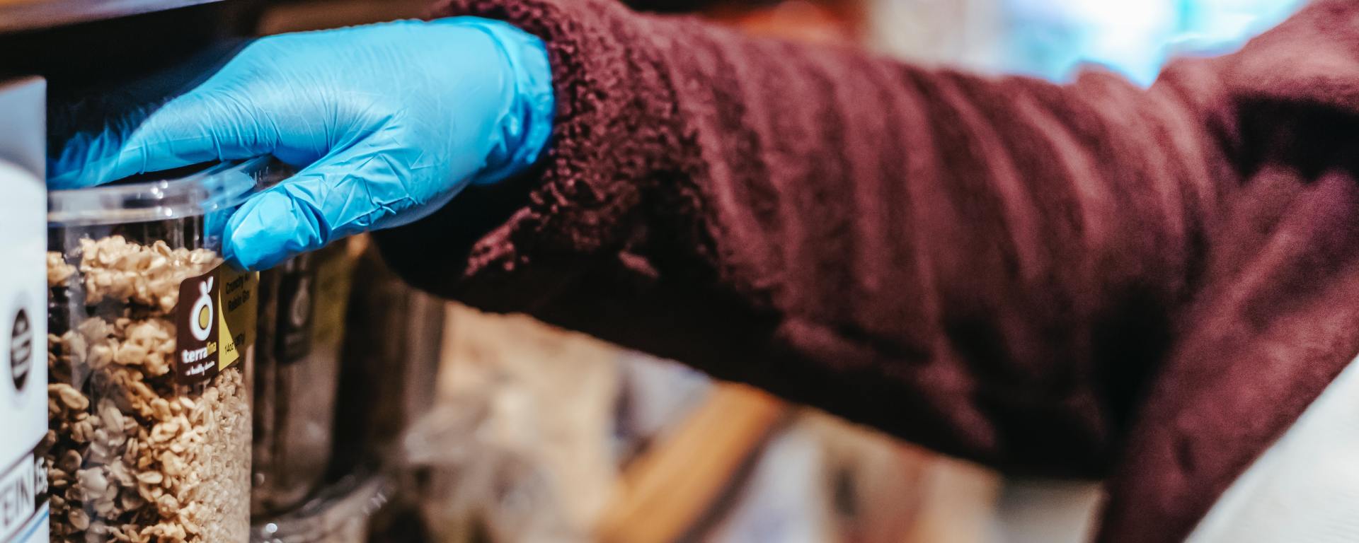 blue-gloved hand picking out a tub of oatmeal in the grocery store