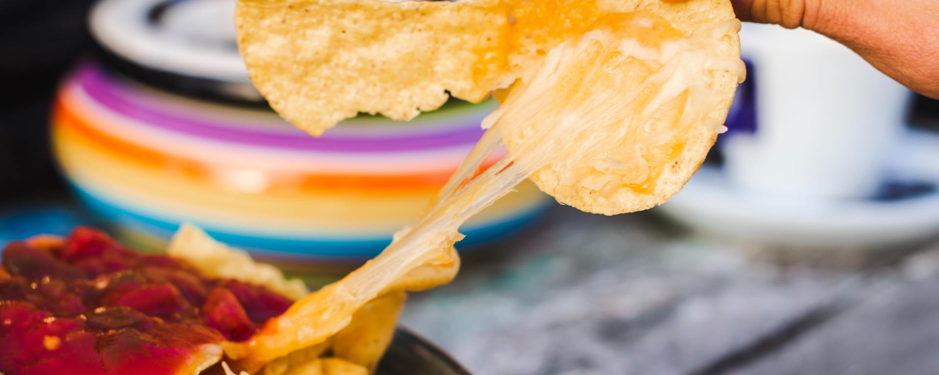 plate of nachos with someone pulling chips away with cheese strung from the plate to the chip