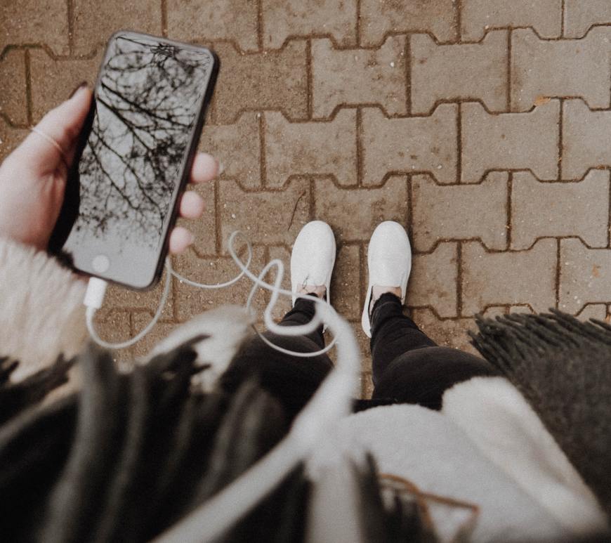 image facing down to someone's white shoes while they hold an iphone with headphones