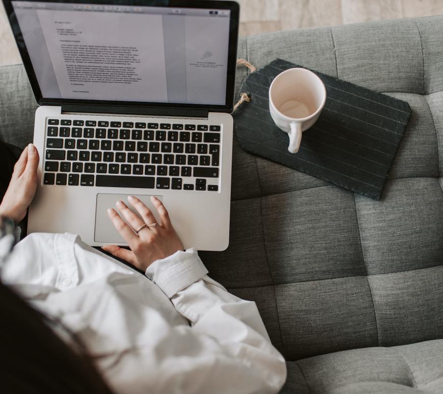woman sitting on couch with computer in lap typing with coffee next to her
