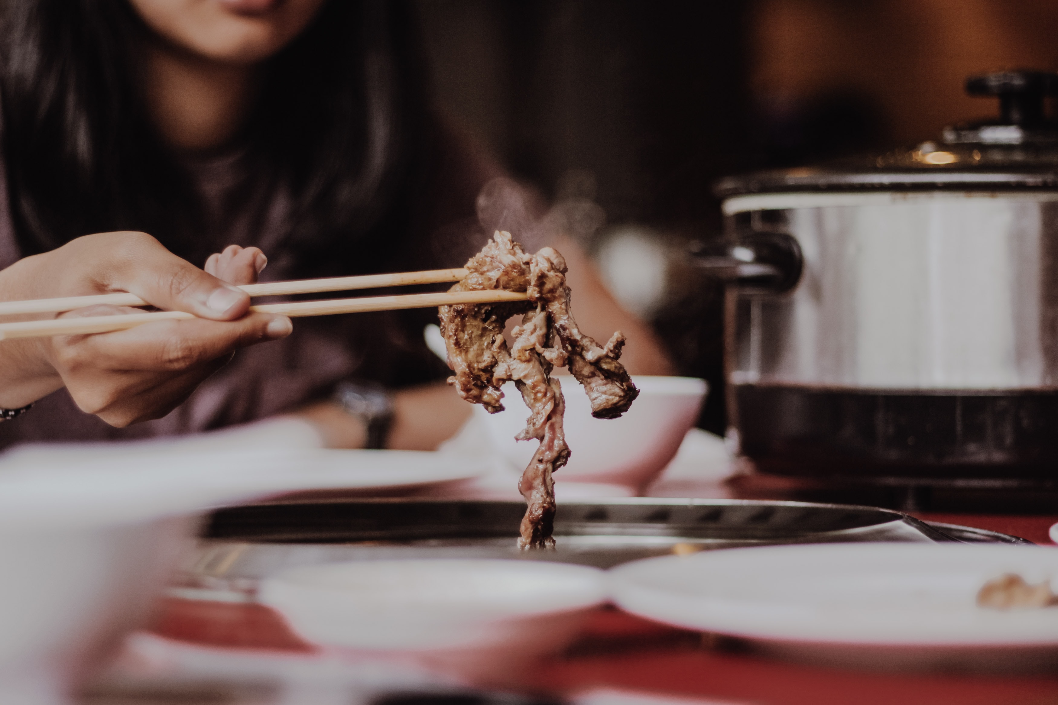 woman holding meat using chopsticks over table with plates and crockpot