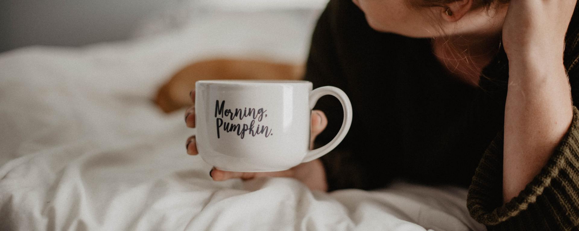 woman laying in bed holding mug that says "morning, pumpkin"