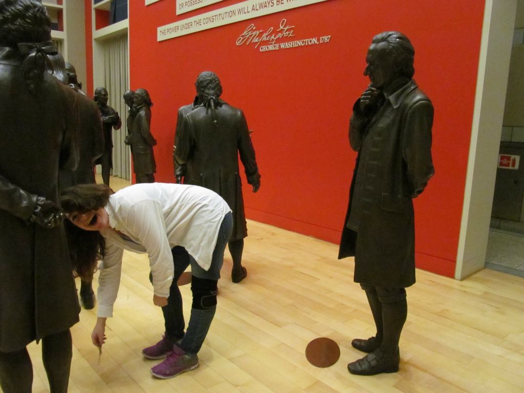 rose bent over and smiling at the camera in front of a bronze statue