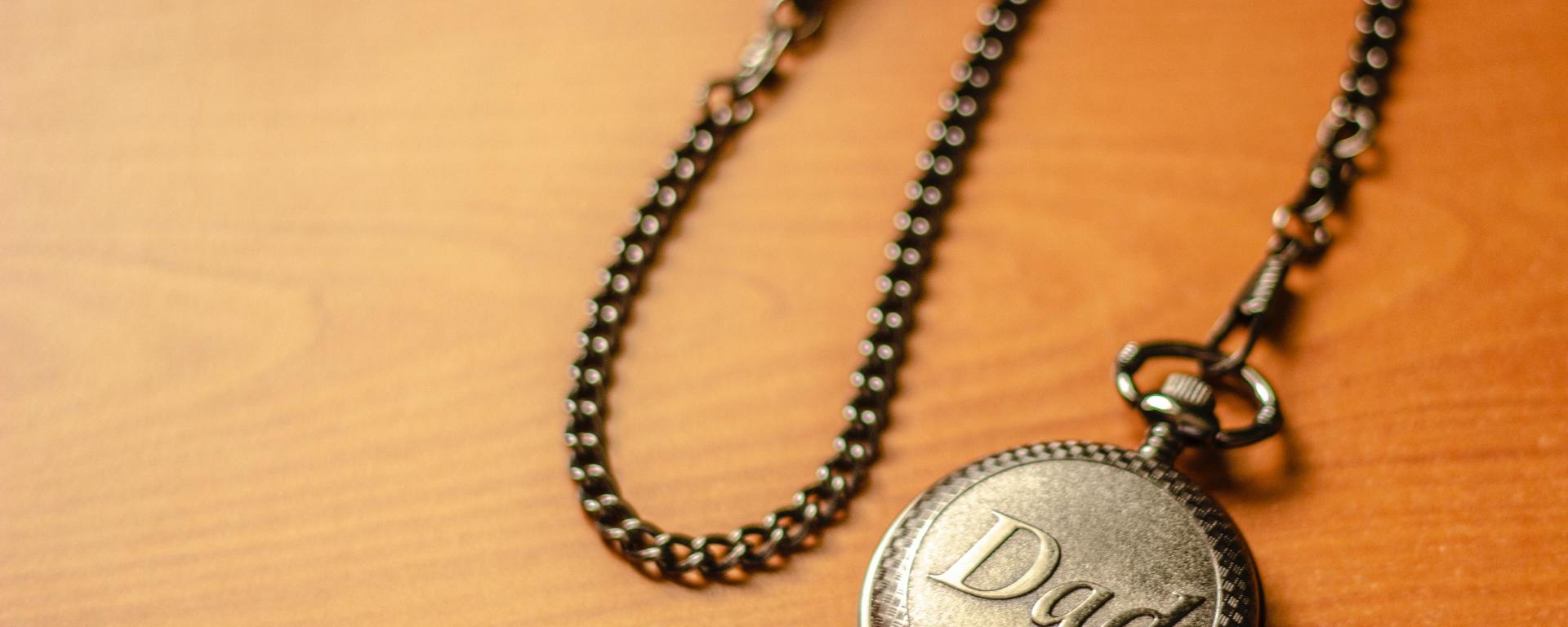 gold pocket watch with "Dad" written on it laying on a wooden surface