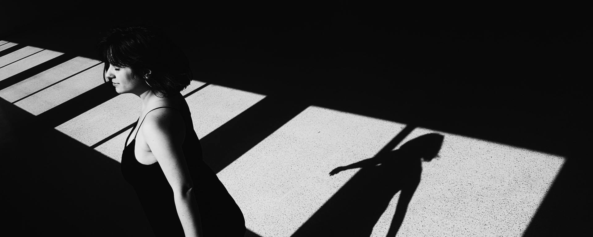 woman standing by windows with arms out, shadow of her on the floor