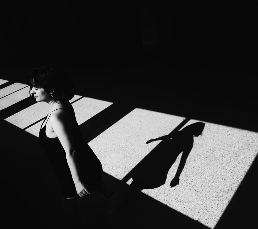 woman standing by windows with arms out, shadow of her on the floor