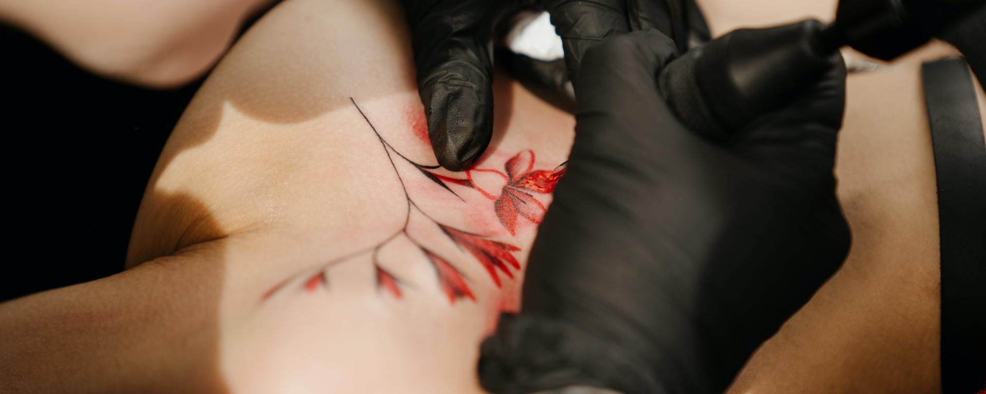 someone tattooing red flowers on another person