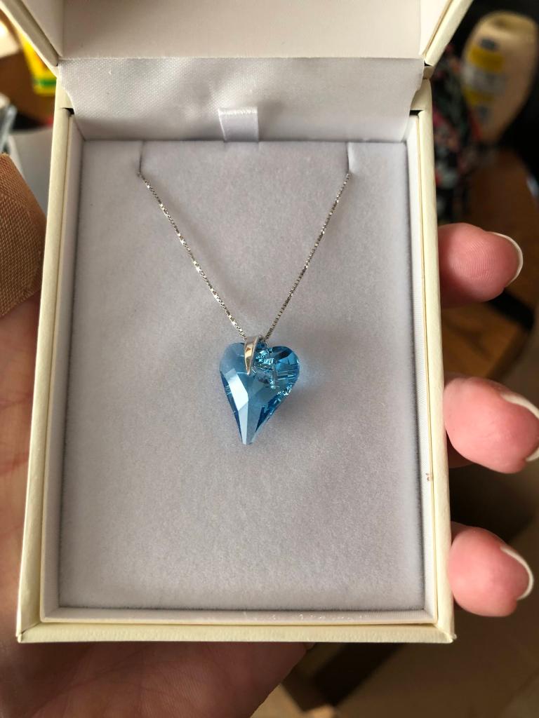 hand holding jewelry box with heart-shaped blue topaz pendant necklace