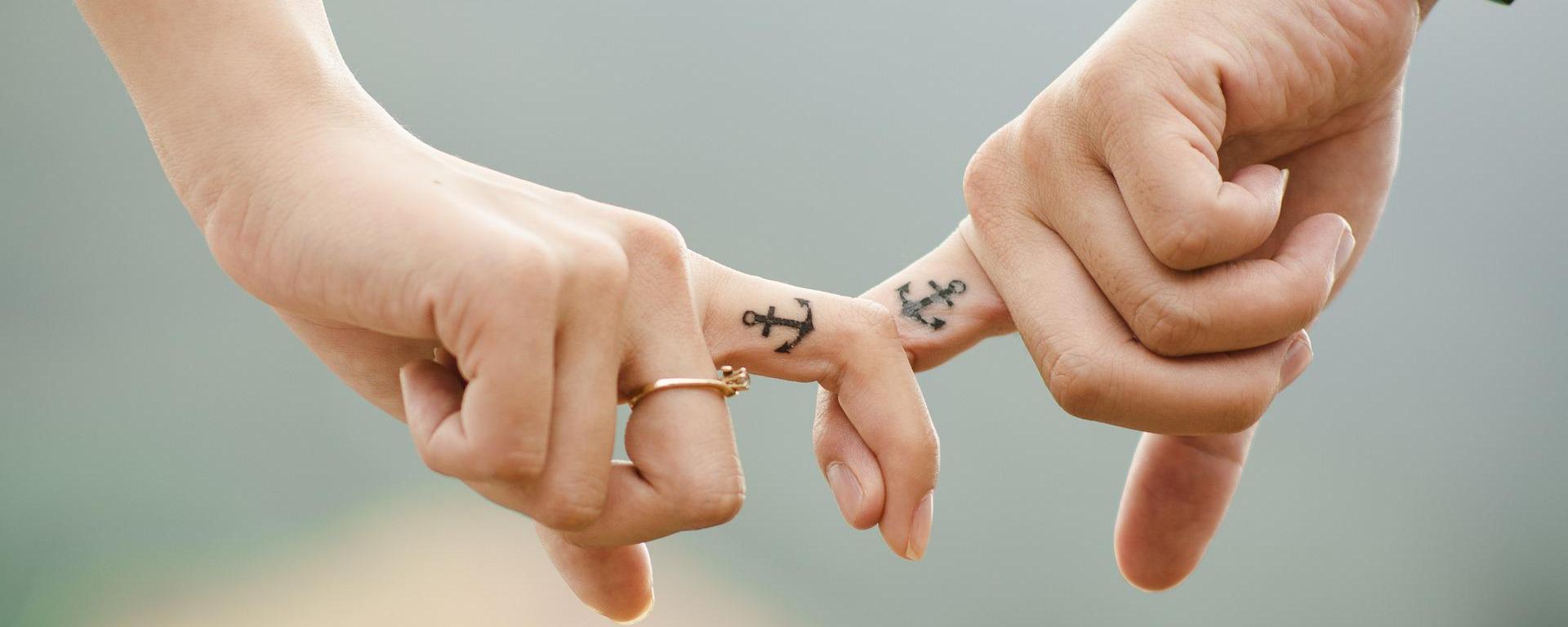 two hands with linked index fingers, both having anchor tattoos