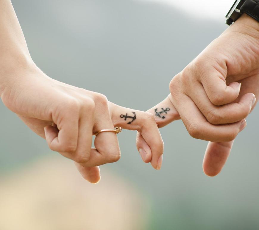 two hands with linked index fingers, both having anchor tattoos