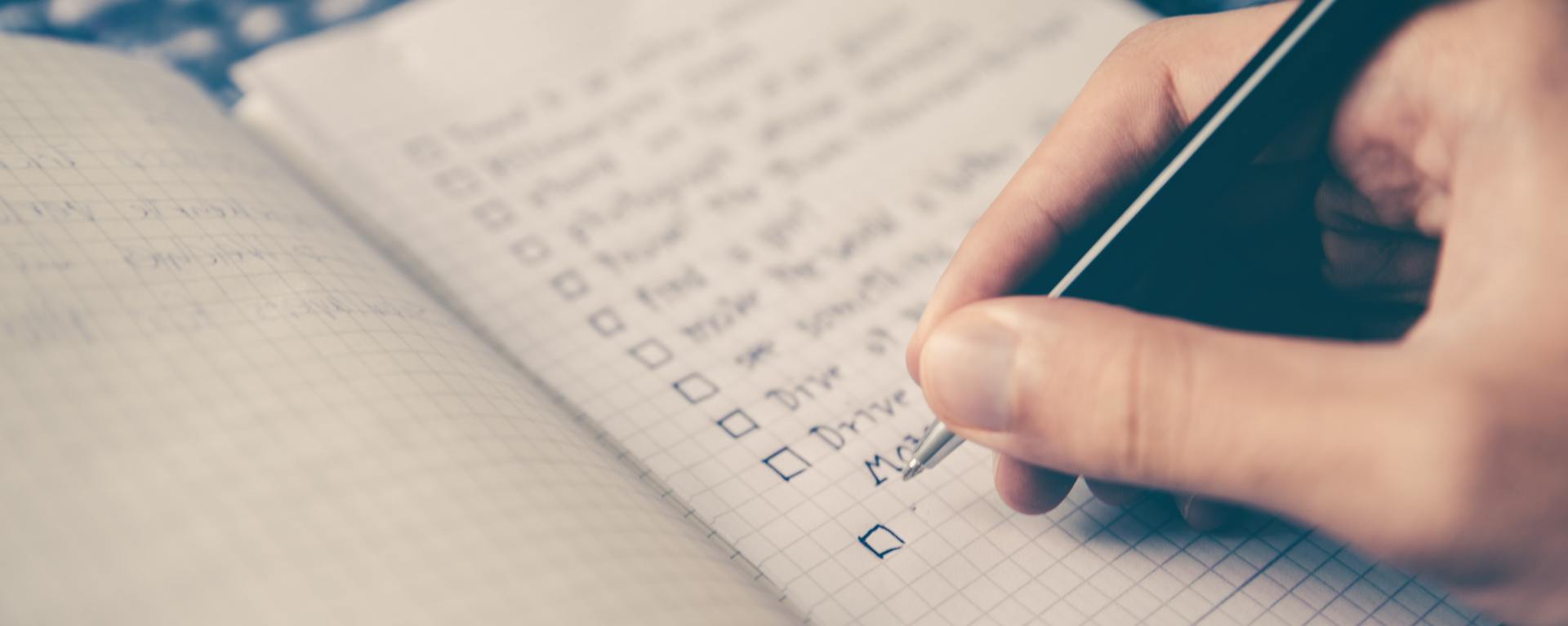 person writing goals with checkboxes in notebook